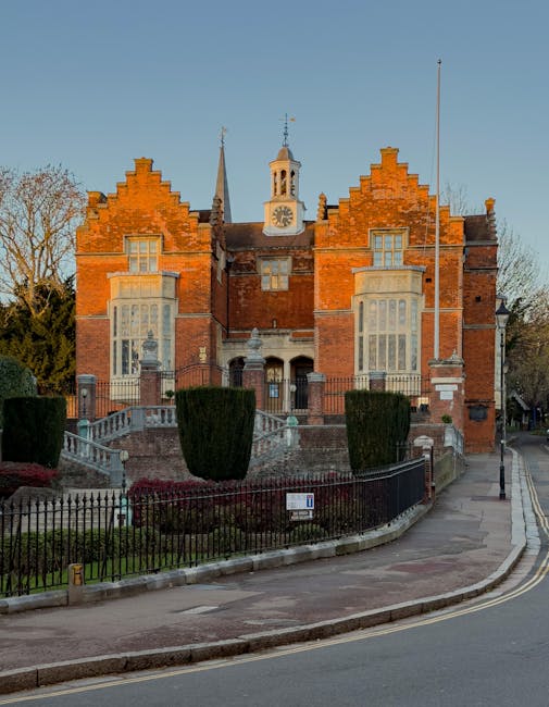 The image depicts a grand red-brick building with classic architectural features, including stepped gables, tall narrow windows, and a central clock tower topped with a weather vane. The building is s