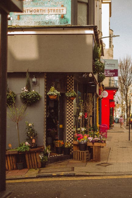 A charming storefront of a flower shop on Harrow high street, decorated with an array of vibrant floral arrangements and hanging baskets. The display includes a variety of fresh flowers such as bright