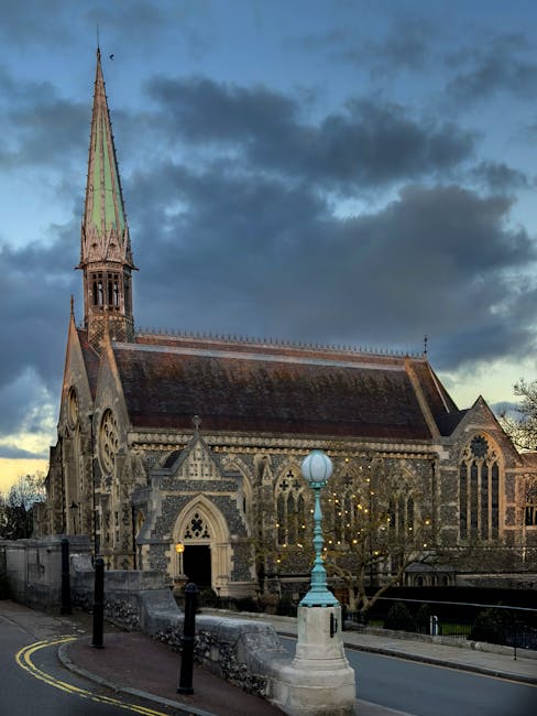 The image depicts a historic stone church with intricate Gothic architectural details, including pointed arch windows and a tall, slender spire topped with a green patina. The church is situated on a